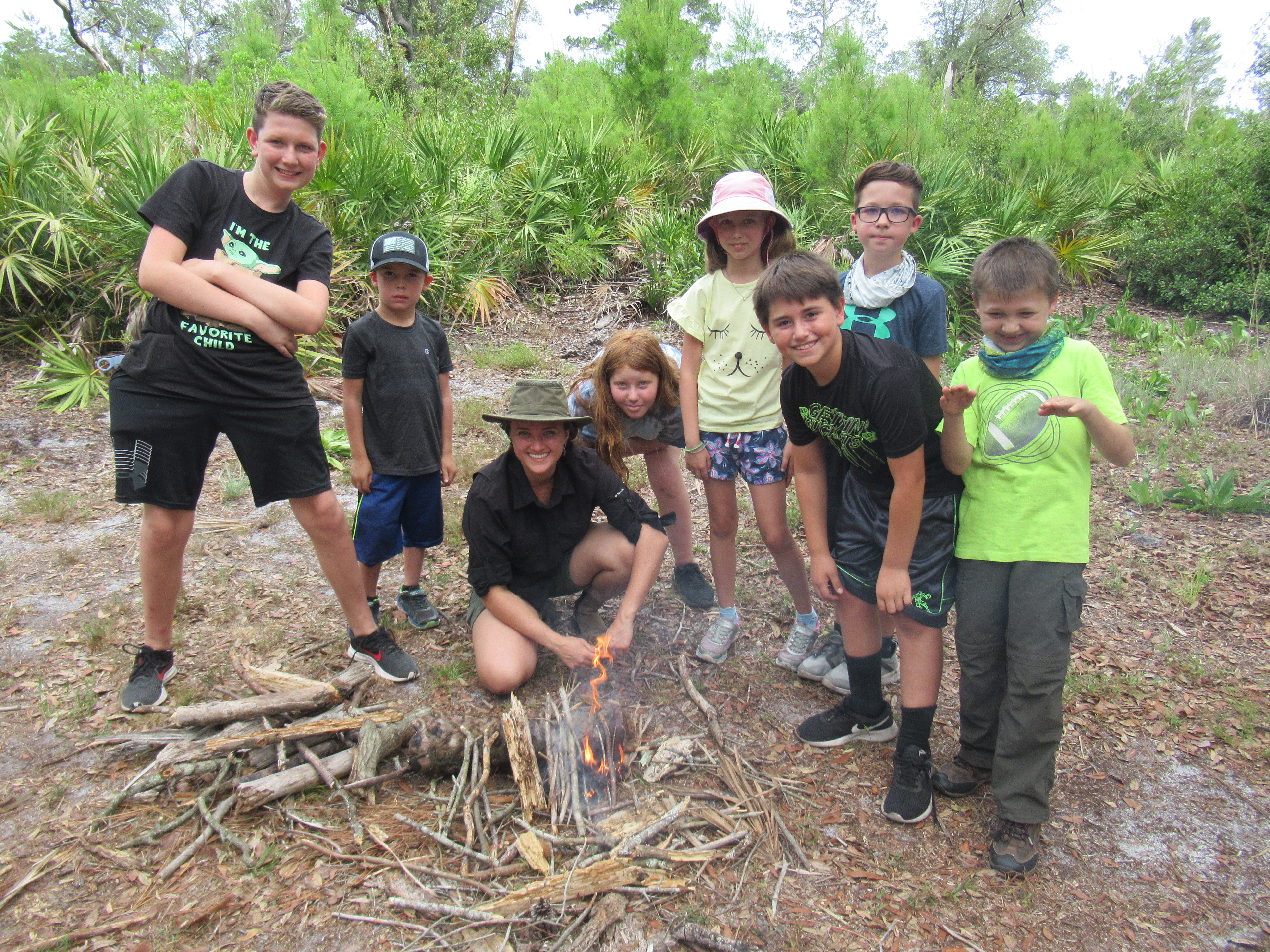 Campers and instructor standing proudly over a fire they started.