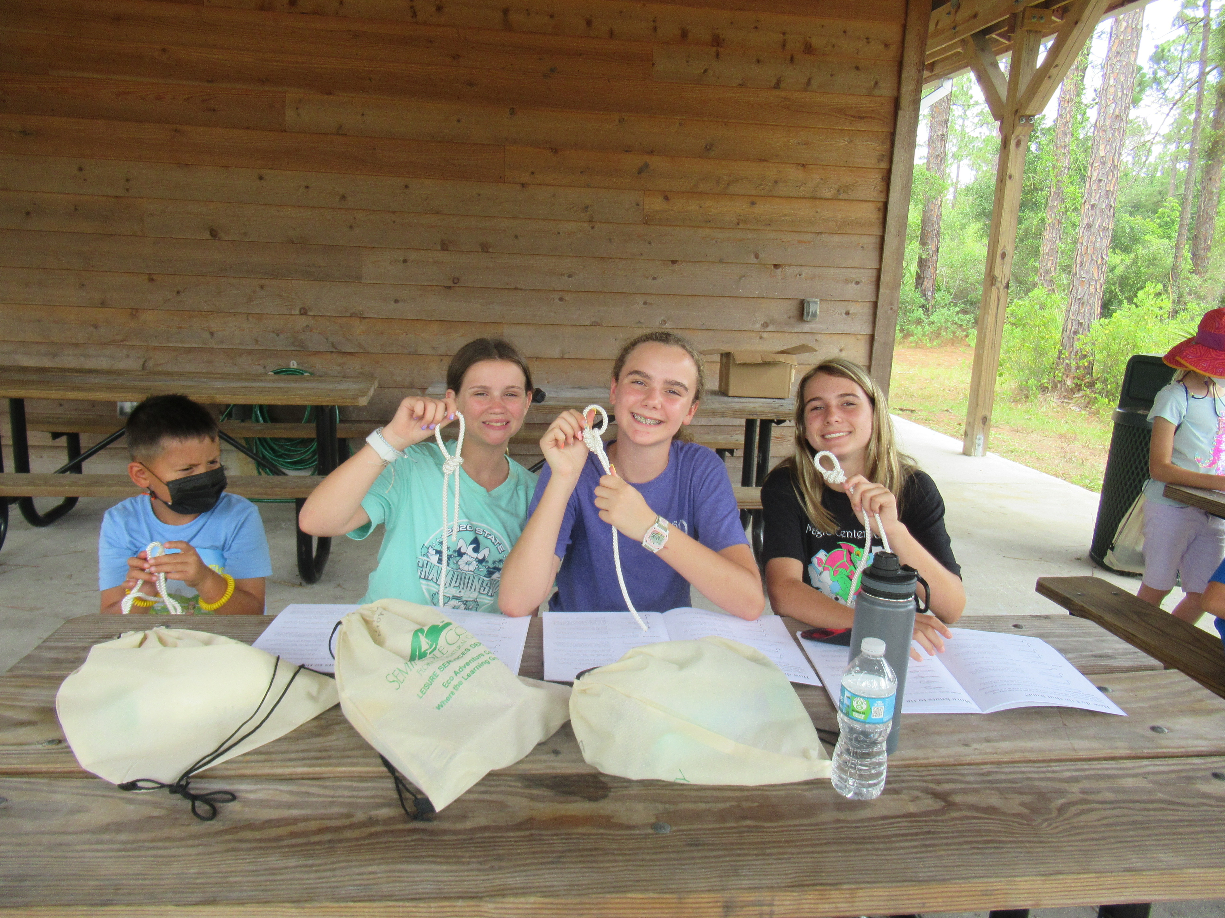 4 children smiling, holding up cords that they are learning to make knots with.