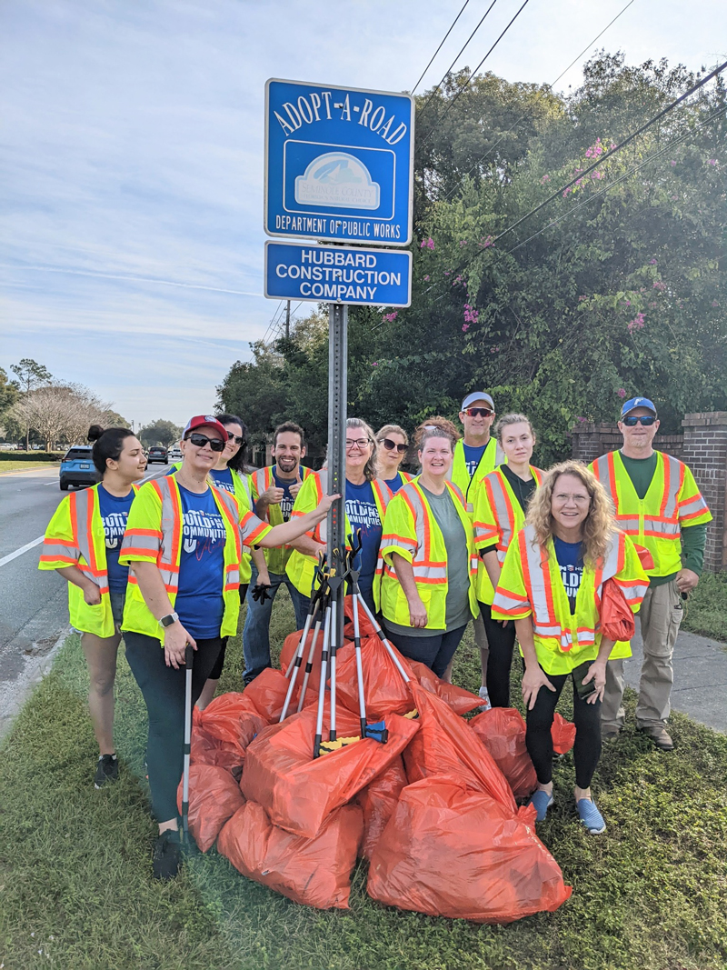 a group of Adopt-A-Road volunteers posing together outside in front of an Adopt-A-Road sign